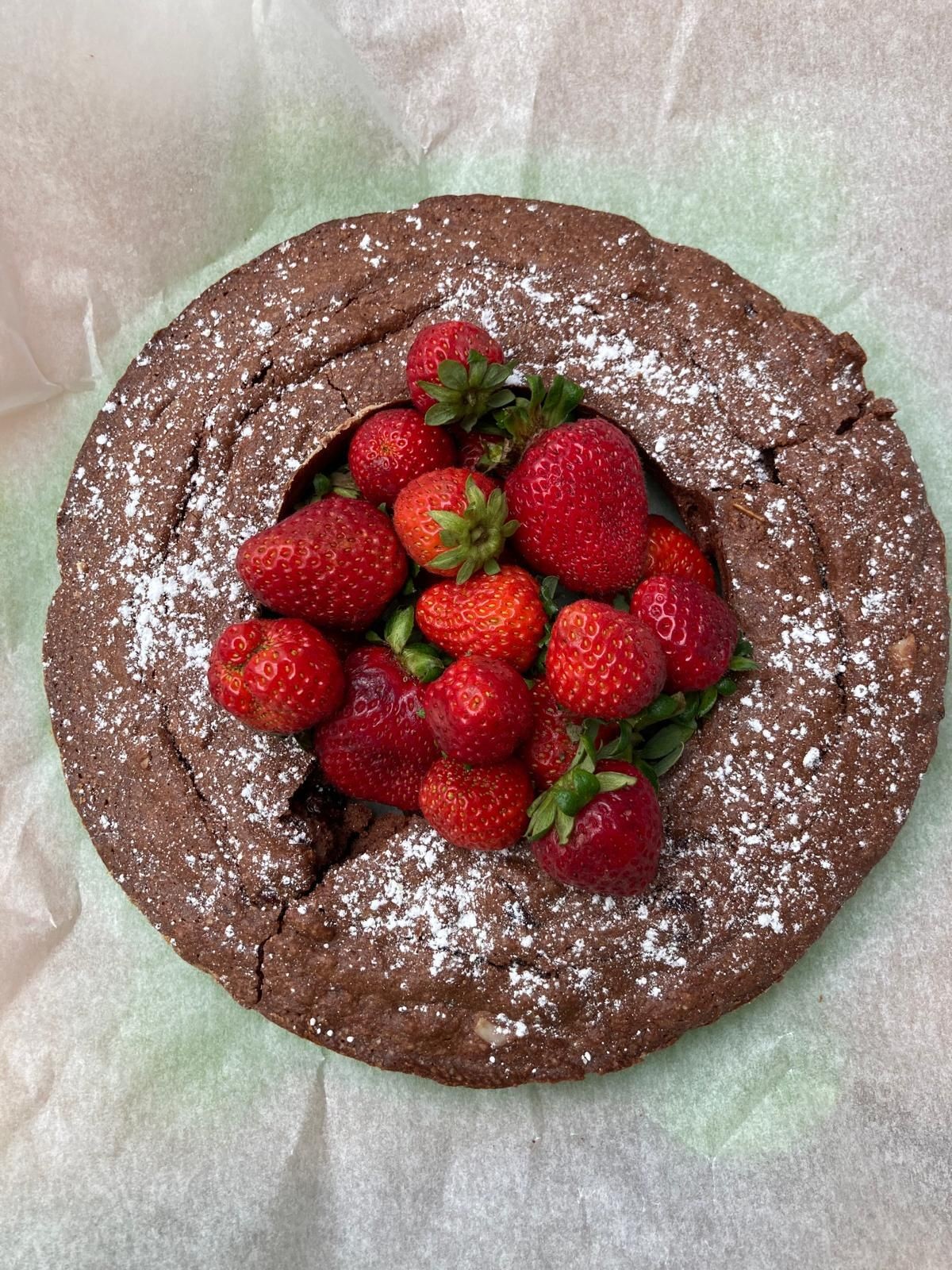 Chocolate cake topped with fresh strawberries and dusted with powdered sugar on parchment paper.