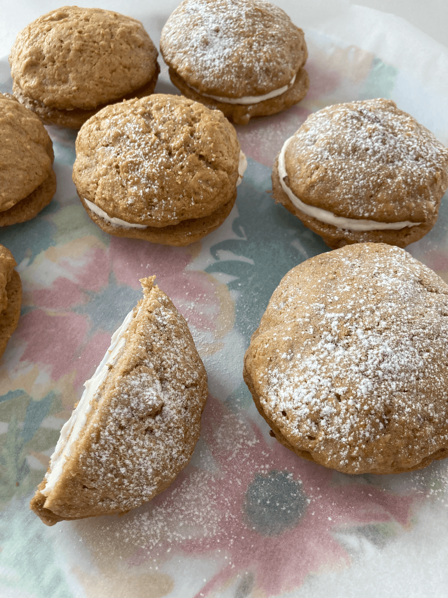 Powdered sugar dusted sandwich cookies with cream filling on floral paper.