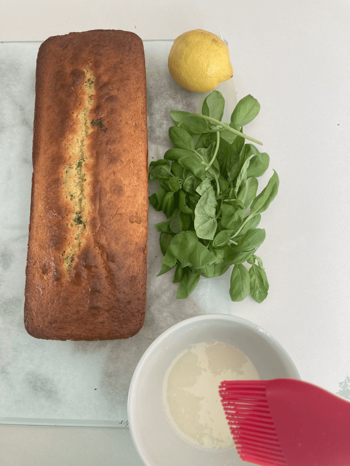 Lemon loaf cake with basil leaves, a lemon, and a red brush in glaze.