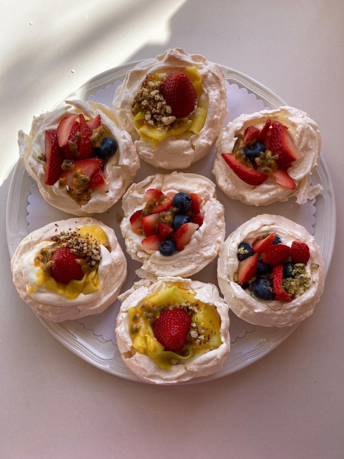 Plate of mini pavlovas topped with strawberries, blueberries, and nuts on a white surface.
