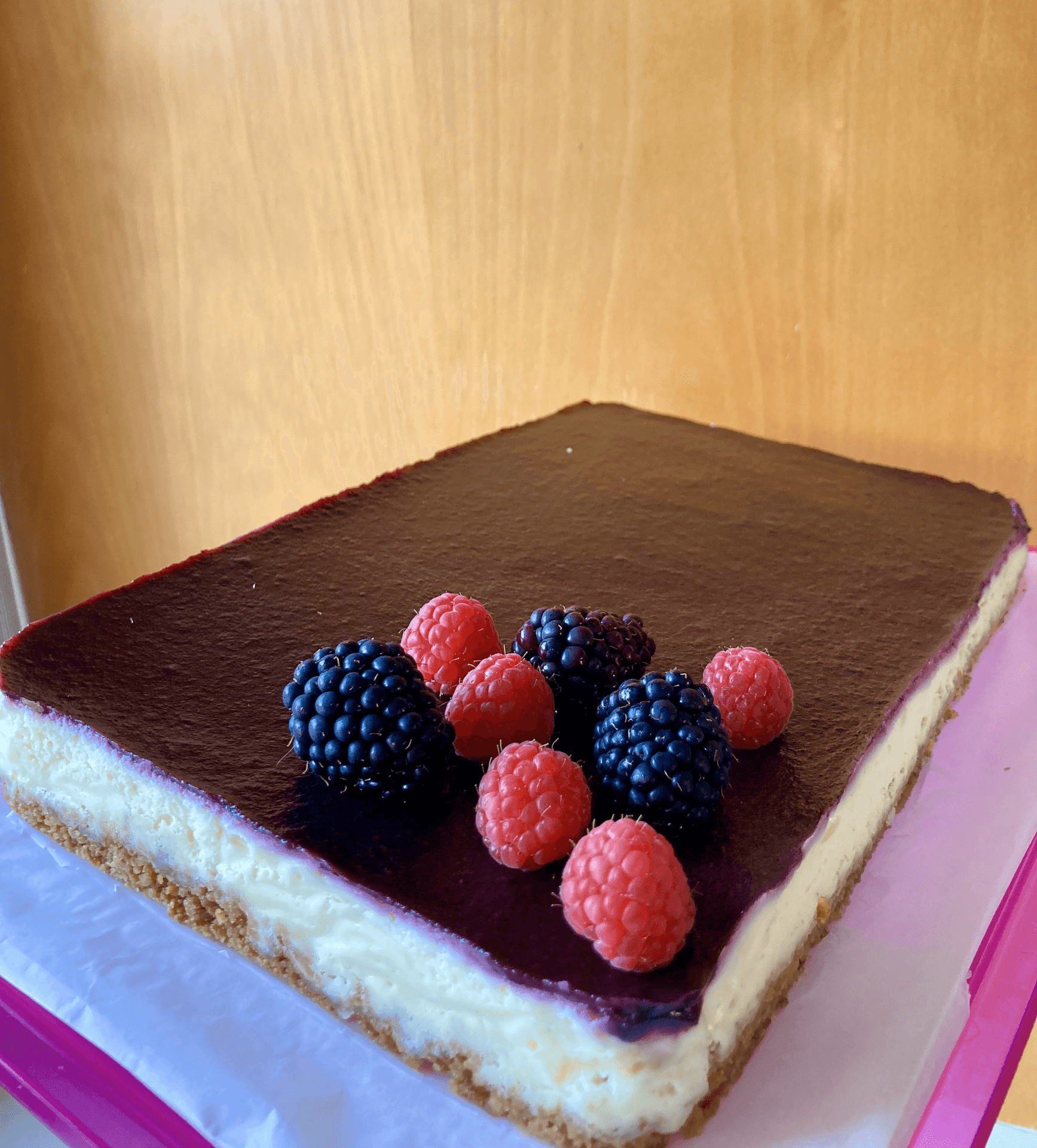 Close-up of a rectangular cheesecake topped with blackberries and raspberries on a wooden background.