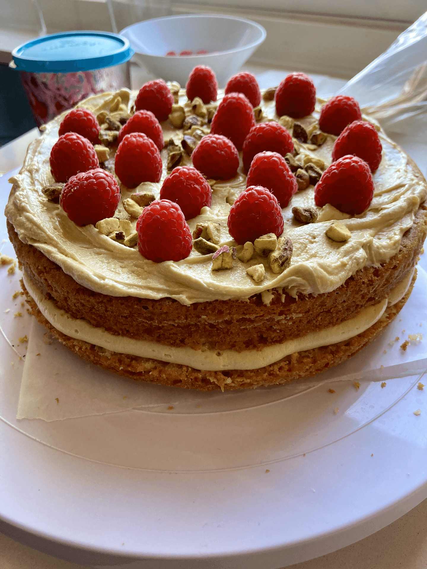 Layered cake topped with raspberries and chopped pistachios on a white plate.