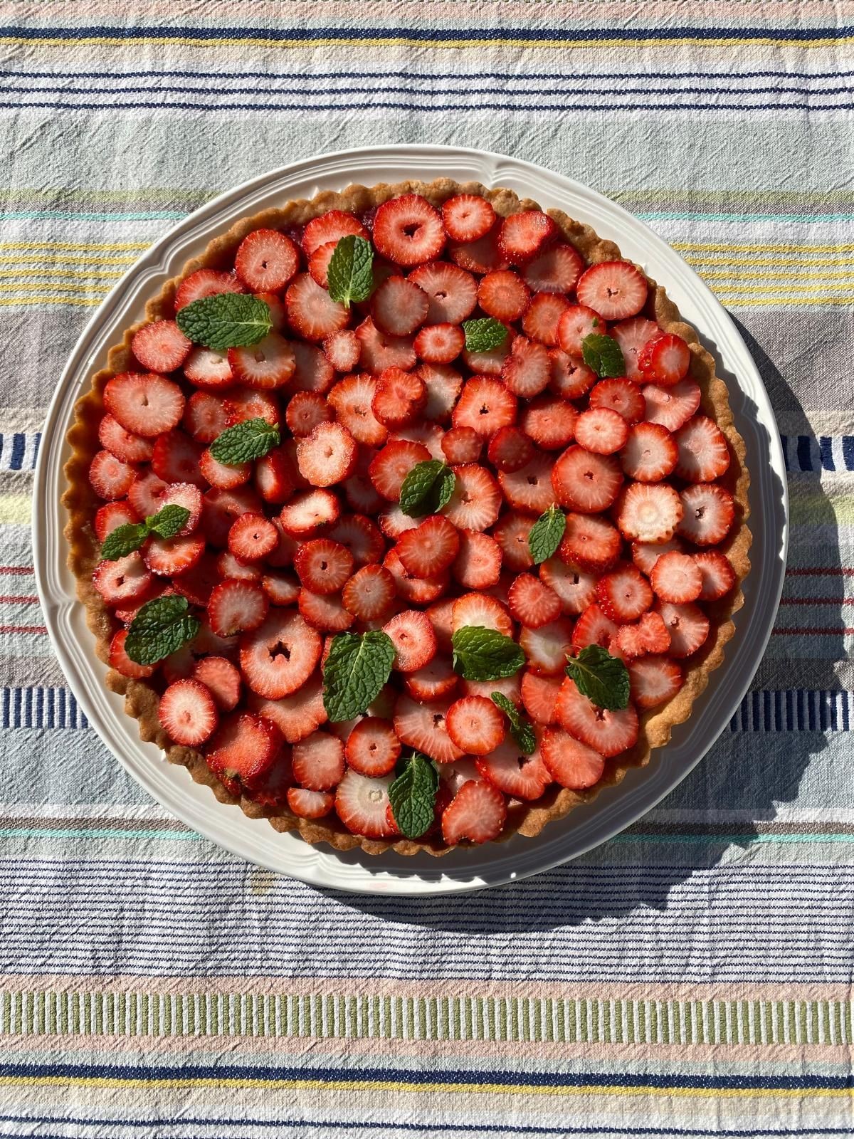 Strawberry tart with mint leaves on a striped tablecloth.