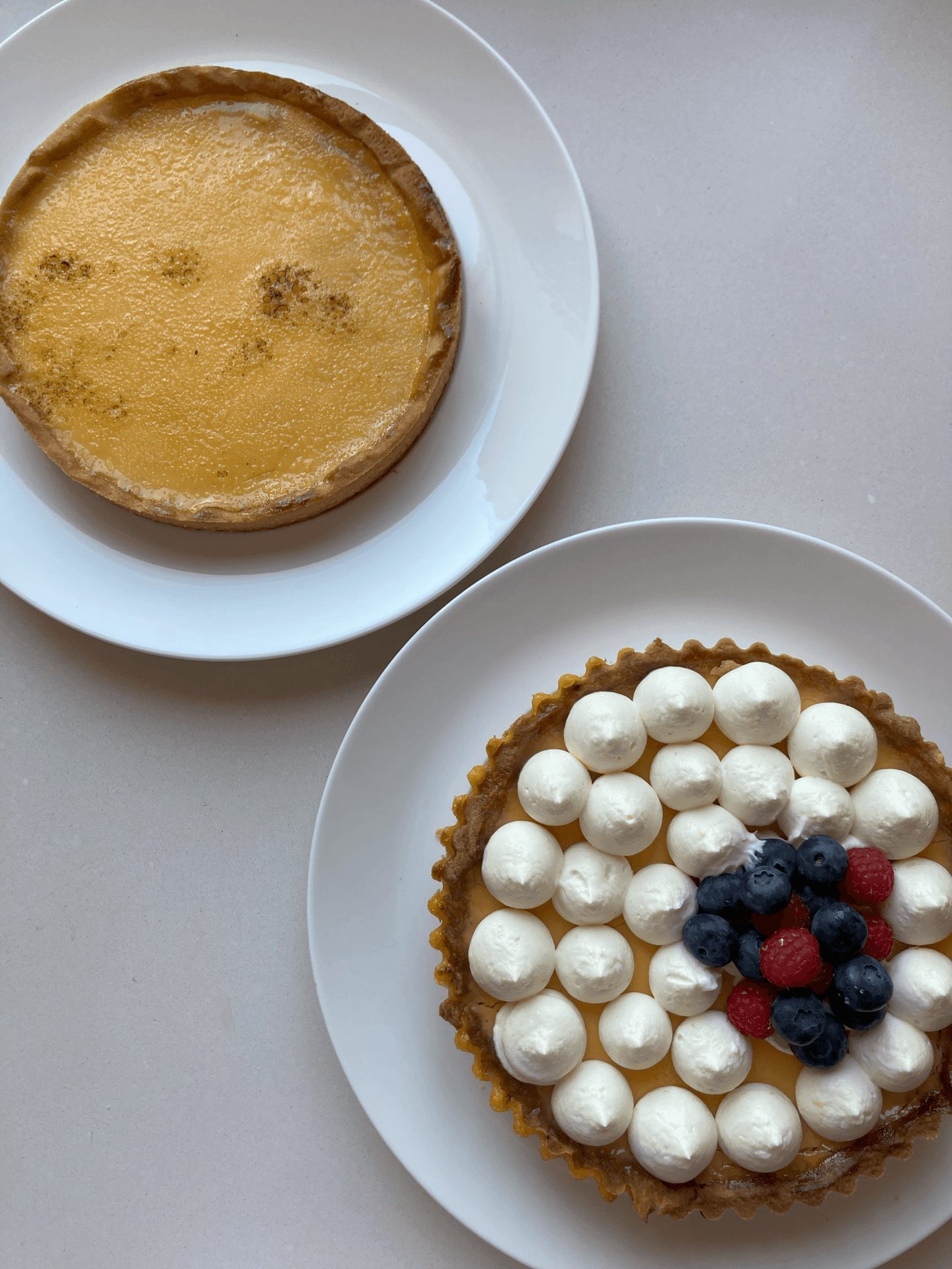 Two desserts on white plates: a lemon tart and a cream-topped tart with berries.
