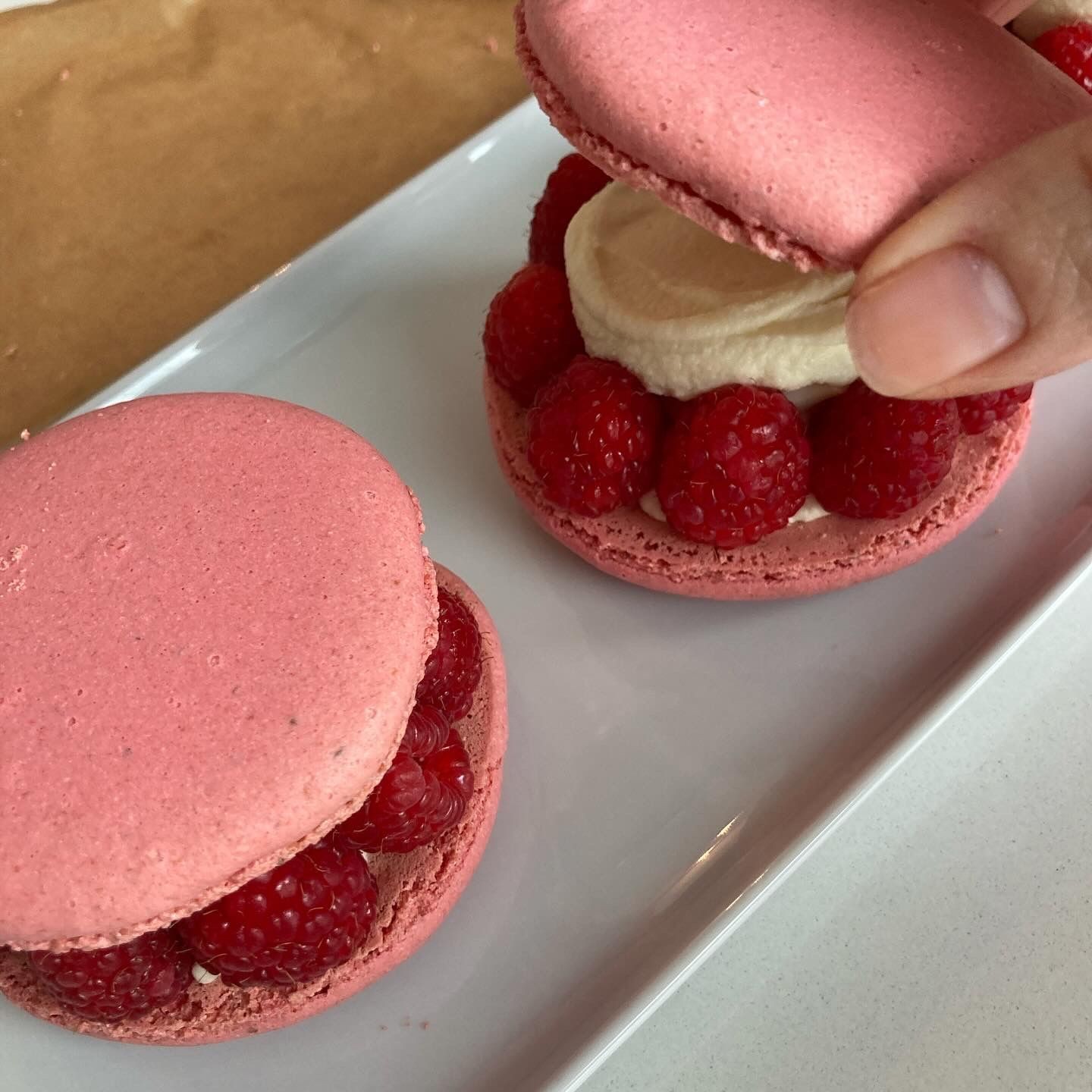 Two pink macarons with raspberries and cream between the shells on a white plate.