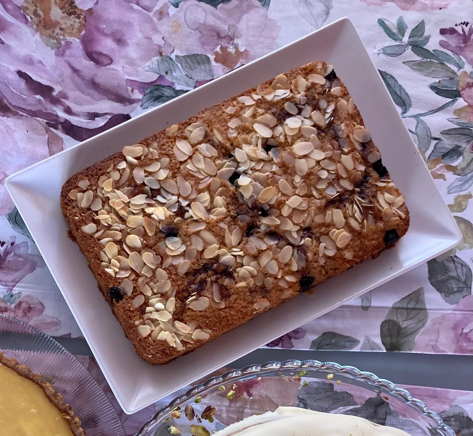 Rectangular almond cake placed on a white plate with a floral tablecloth background.