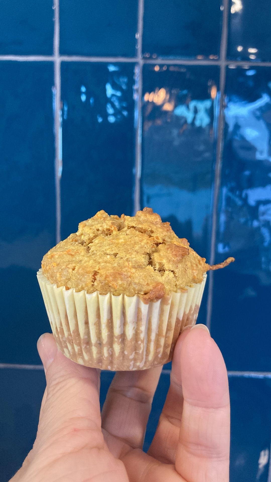 Hand holding a muffin against a blue tiled background.