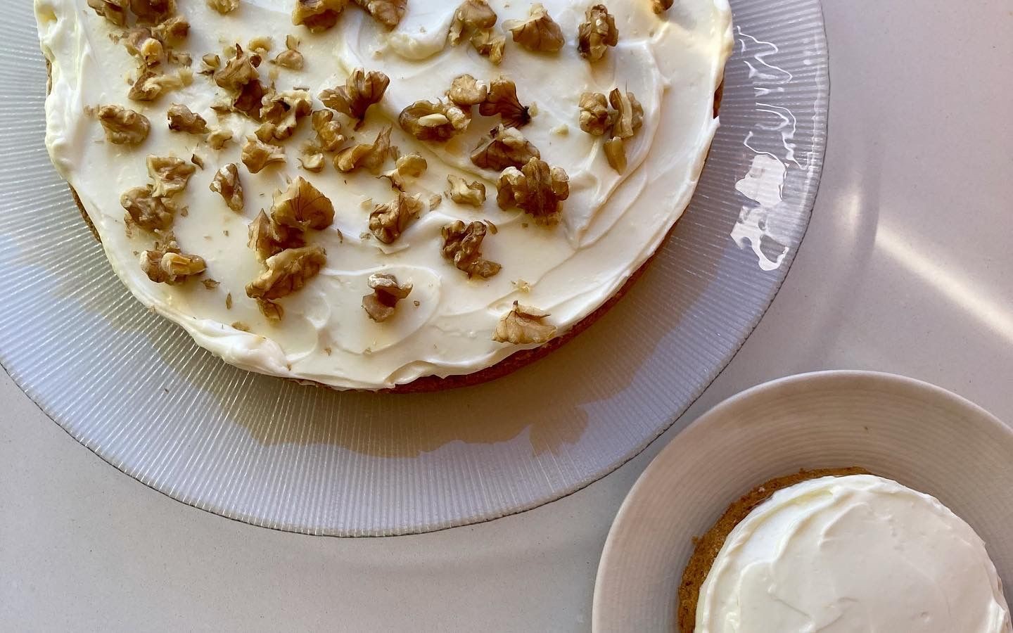Cake covered with white frosting and walnuts, next to a small frosted cake on plates.