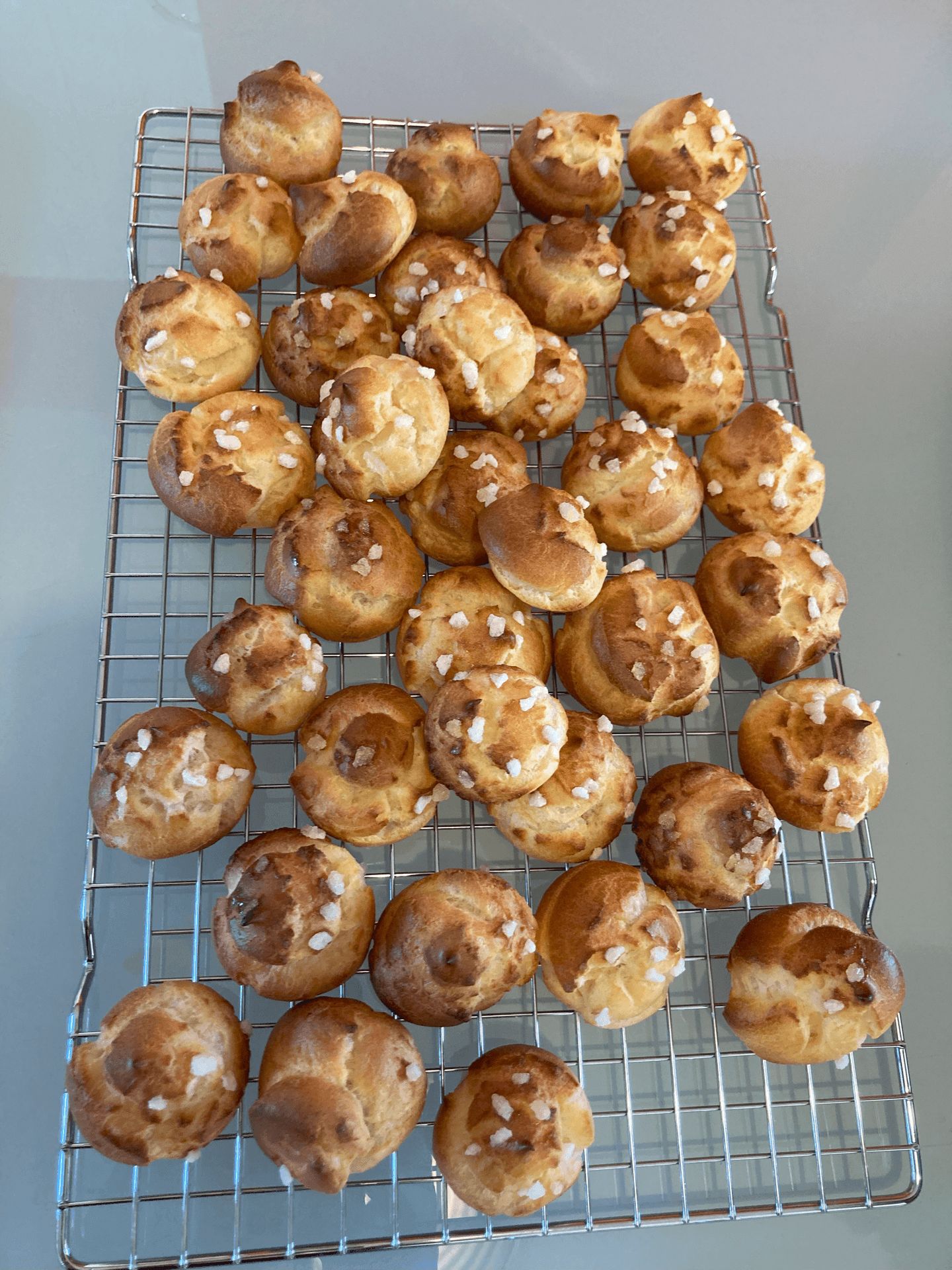 Tray of choux pastry puffs with sugar crystals on a cooling rack.