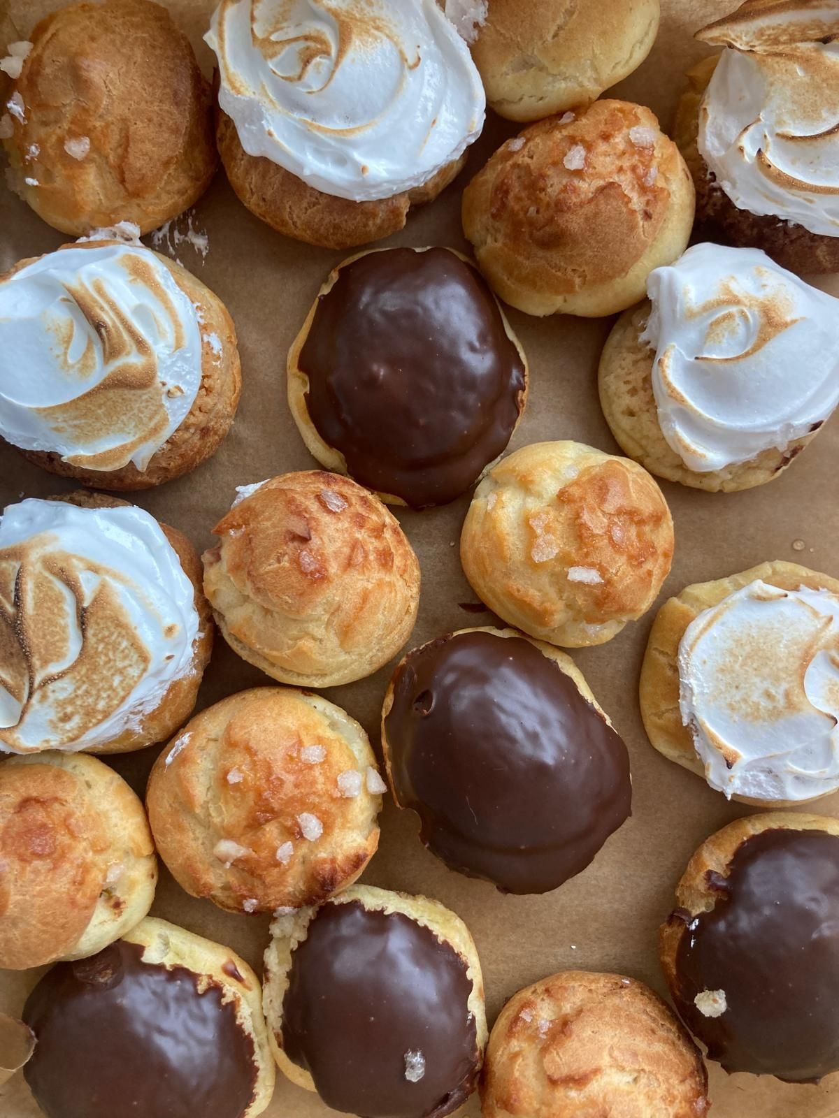 Assorted cream puffs with chocolate glaze and whipped cream toppings on a tray.