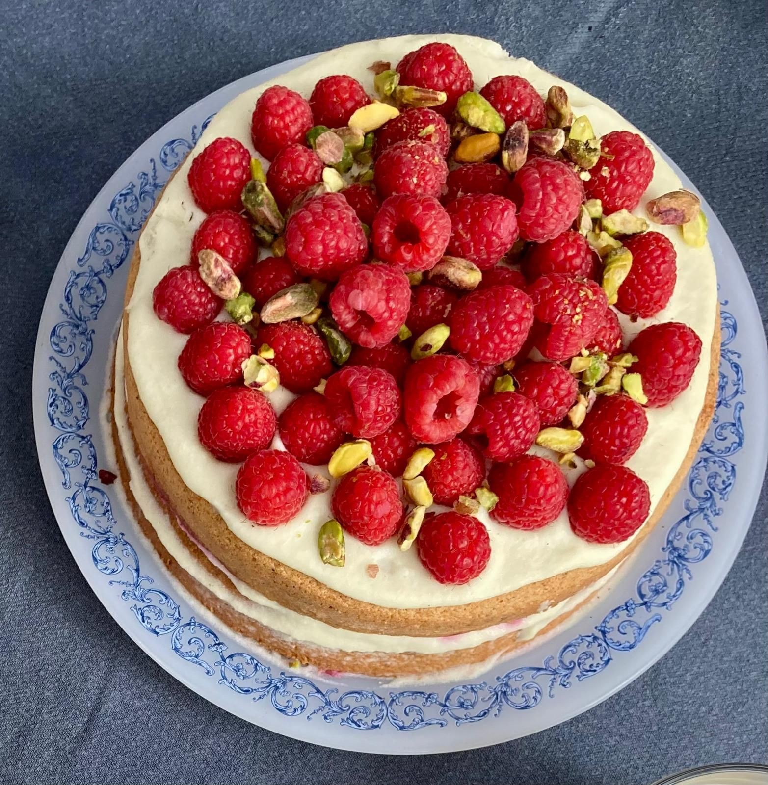 Layer cake topped with raspberries and pistachios on a decorative blue plate.