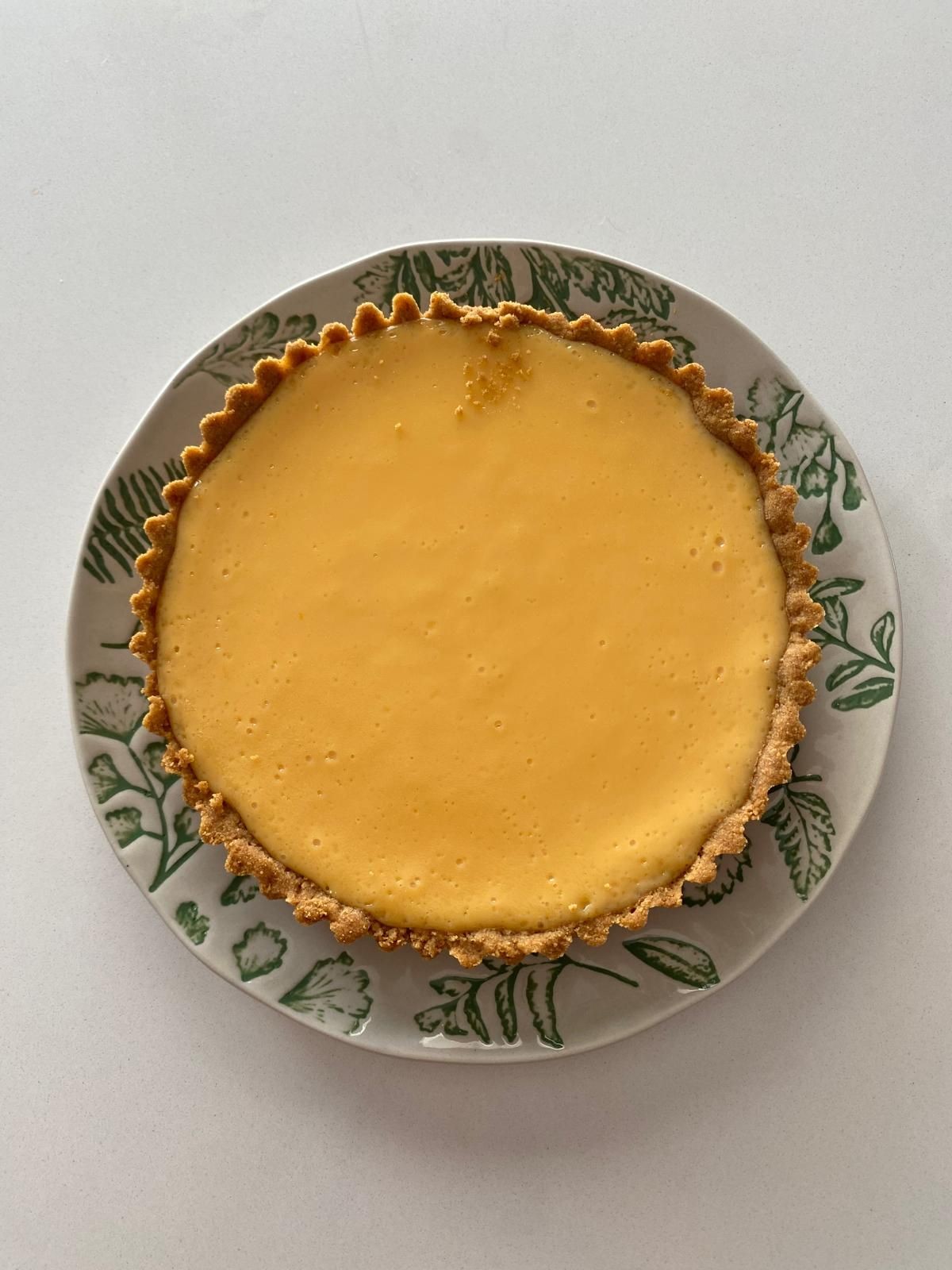 Top view of a lemon tart on a decorative plate with green leaf patterns.