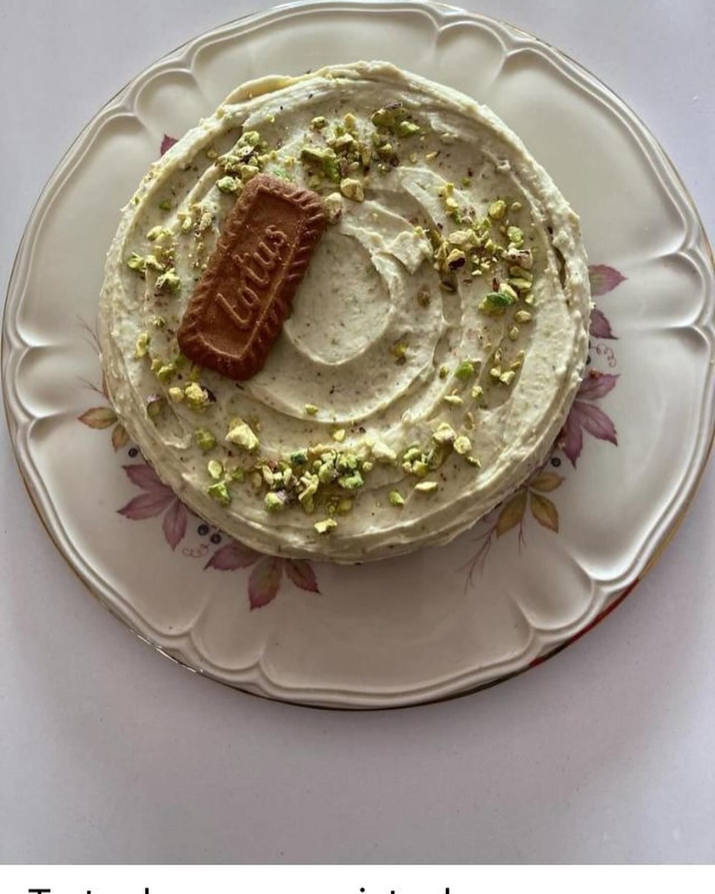 Round cake with pistachio topping and a biscuit on floral plate.