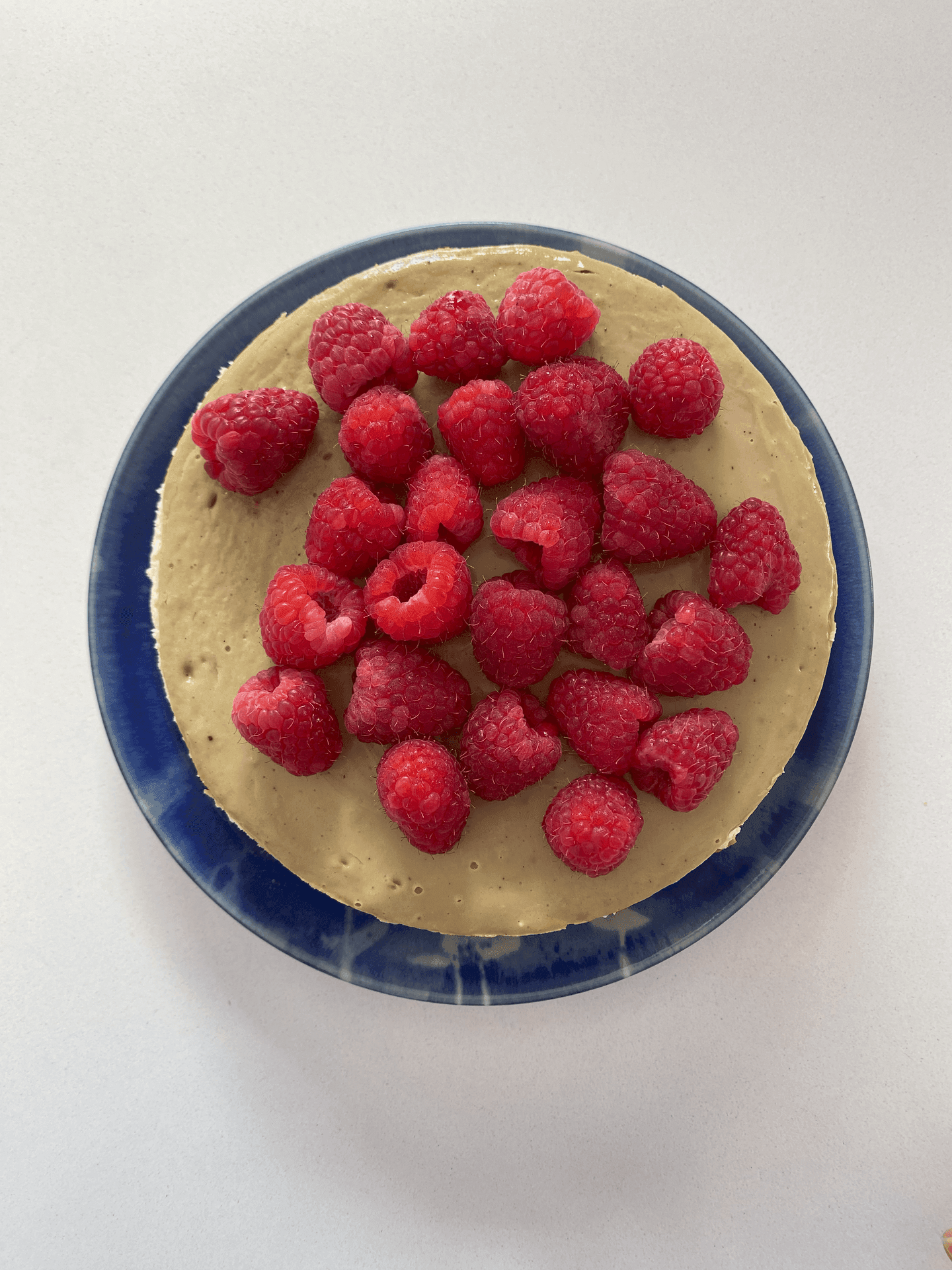 Top view of a cake topped with fresh raspberries on a blue plate against a light background.