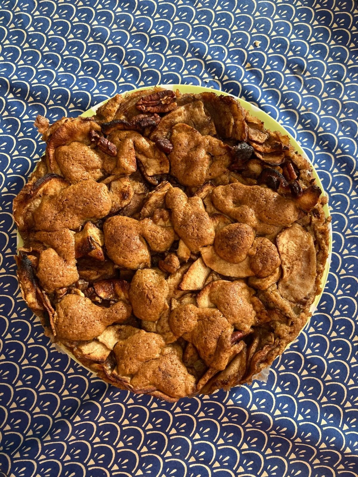 Homemade apple pie with a rustic crust on blue patterned tablecloth.