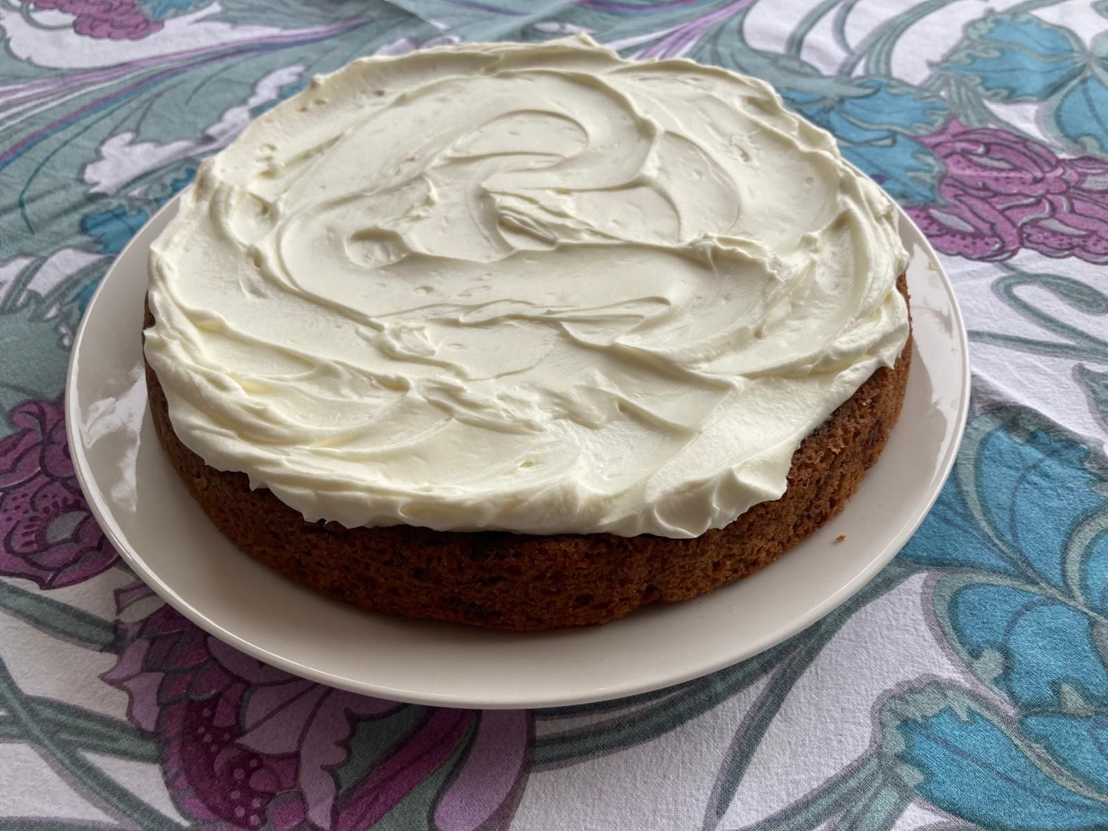 Carrot cake with cream cheese frosting on a white plate.
